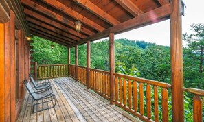 A wooden deck with a railing, a bench, and a view of a forested landscape. - Splash N Around (Sevierville)