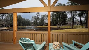 Eine überdachte Terrasse mit Adirondack-Stühlen und einem Tisch, mit Blick auf einen Teich und ein bewaldetes Gebiet.