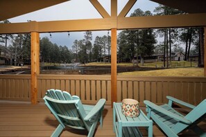 Eine überdachte Terrasse mit Adirondack-Stühlen und einem Tisch, mit Blick auf einen Teich und ein bewaldetes Gebiet.