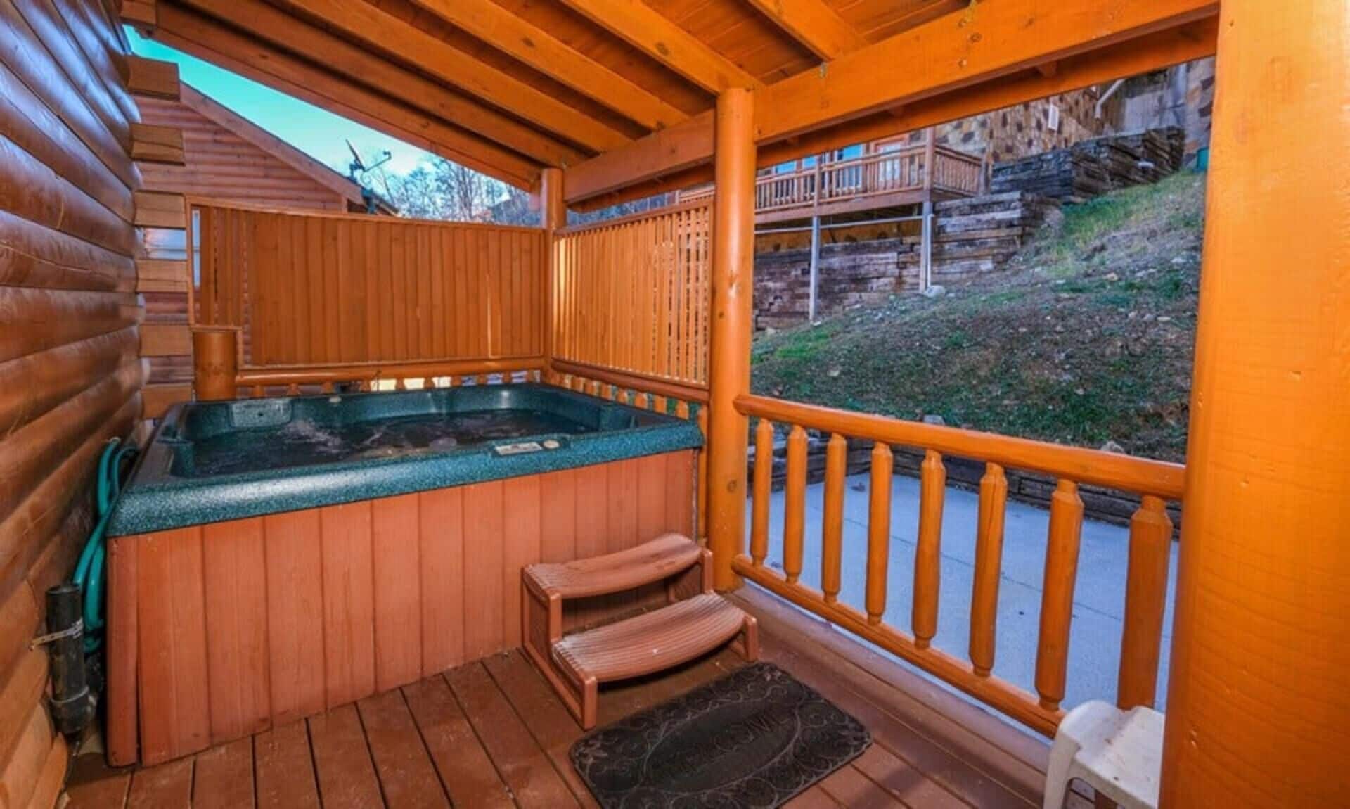Ein Holz-Whirlpool mit Stufen, eine Holzterrasse und Blick auf eine Holzhütte.