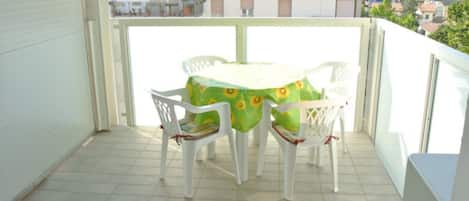 A balcony with a table and chairs, a tiled floor, and a view of buildings.