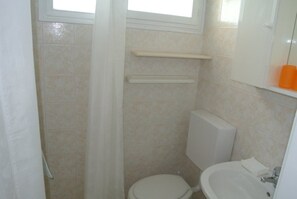 Een badkamer met toilet, wastafel, raam en douchegordijn.