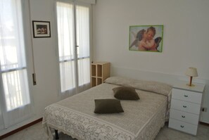 Een slaapkamer met een bed, kussens, een nachtkastje, een lamp en een schilderij aan de muur.