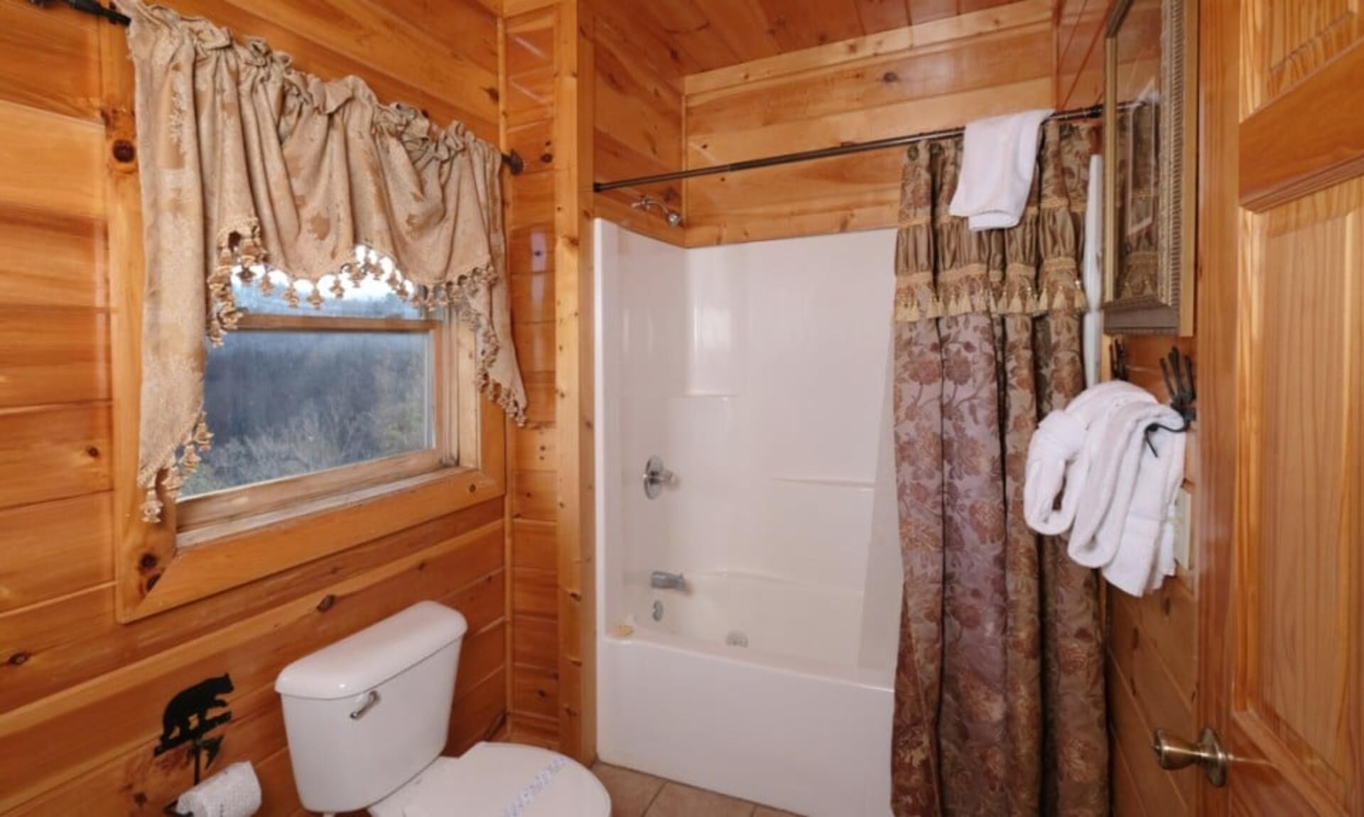 A wooden cabin bathroom with a toilet, bathtub, and shower curtain.