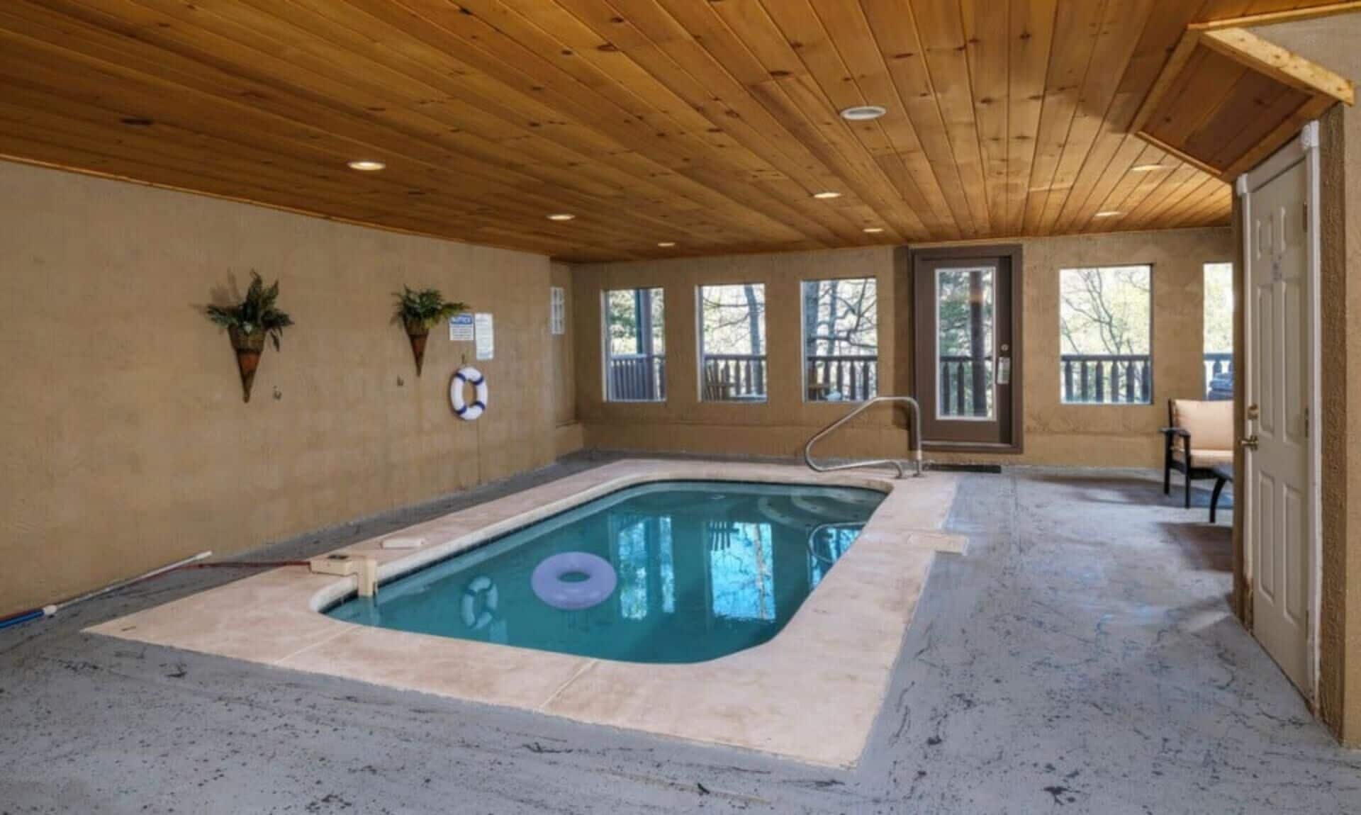 Ein Innenpool mit Holzbalkendecke, Fenstern und einer Tür, die nach draußen führt.