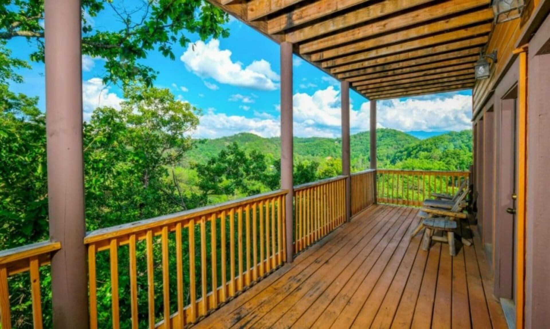 A wooden deck with a railing, a bench, and a view of green hills.