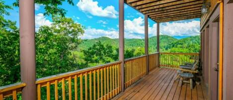 A wooden deck with a railing, a bench, and a view of green hills.