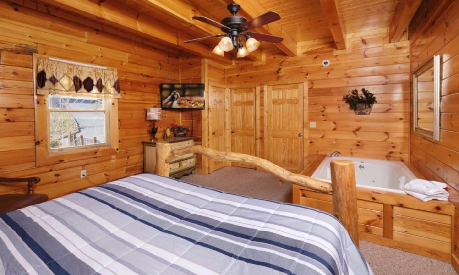 A log cabin bedroom with a bed, a wooden desk, a bathtub, and a ceiling fan.
