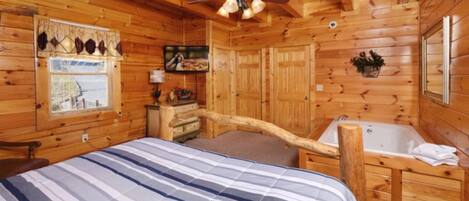 A log cabin bedroom with a bed, a wooden desk, a bathtub, and a ceiling fan.
