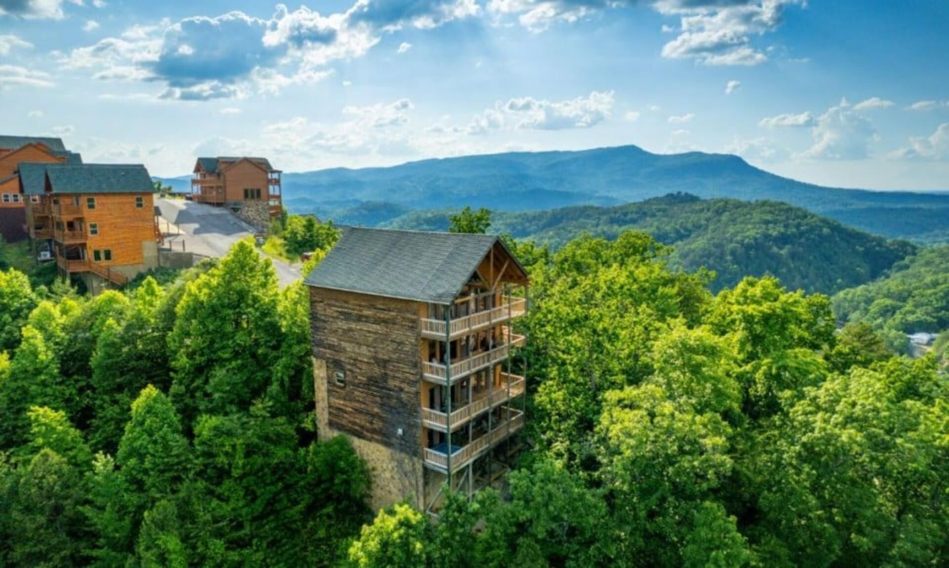 Une cabane en bois dotée d’un balcon, entourée d’une forêt dense et avec des montagnes en arrière-plan.