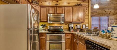 Una cocina con armarios de madera, electrodomésticos de acero inoxidable, lavavajillas y una ventana con persianas.
