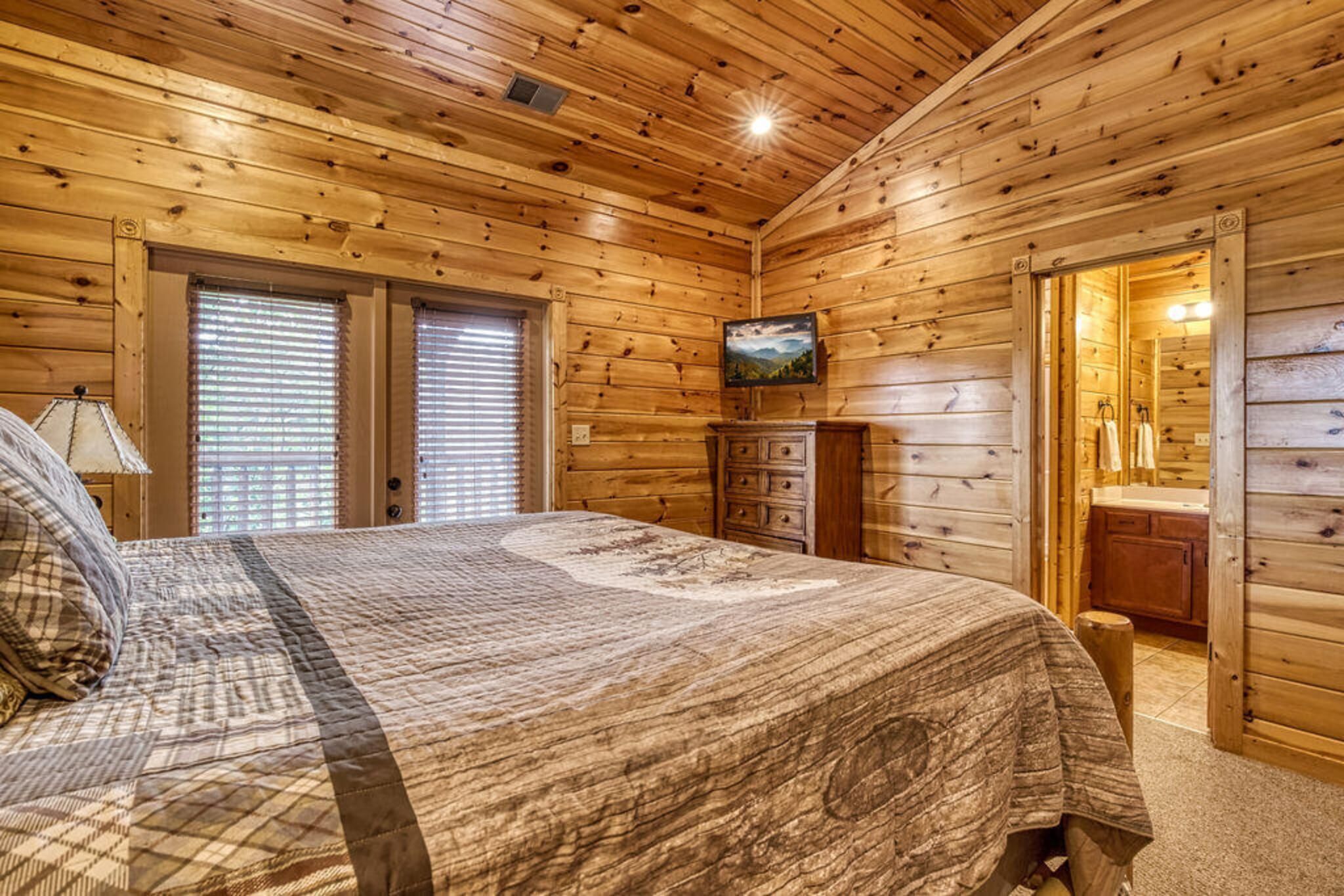 A wooden cabin bedroom with a bed, dresser, and a television on the wall.