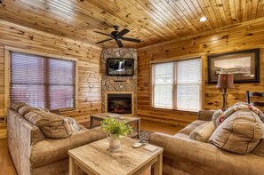 Ein rustikales Holzhaus-Interieur mit Kamin, Holzwänden, Deckenventilator und zwei Sofas.