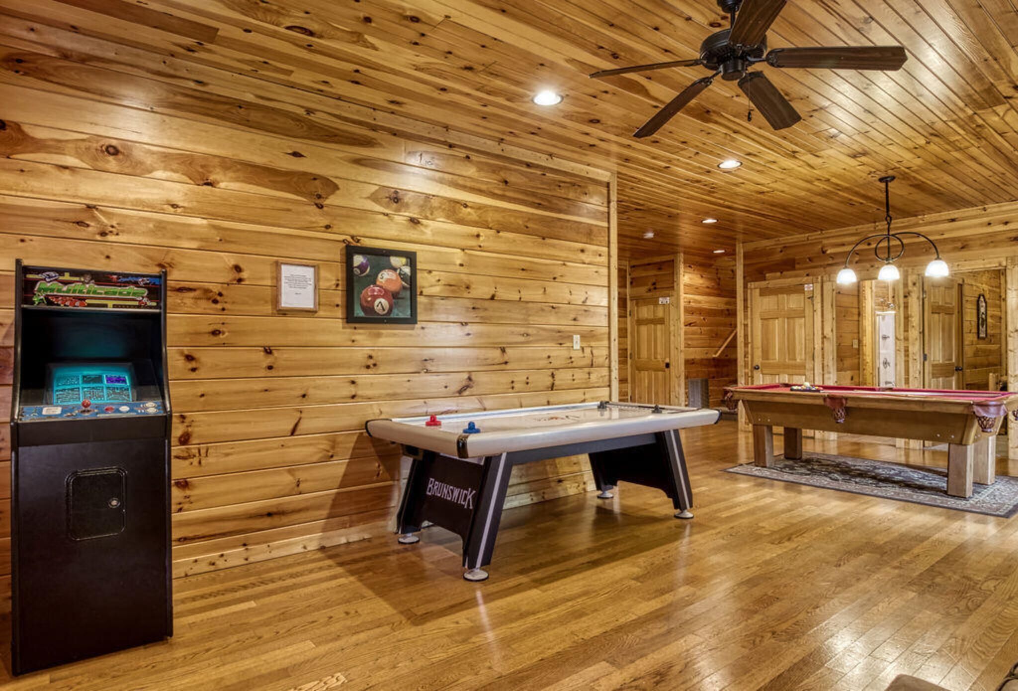 Una sala con piso de madera, mesa de billar, mesa de futbolín y jukebox.