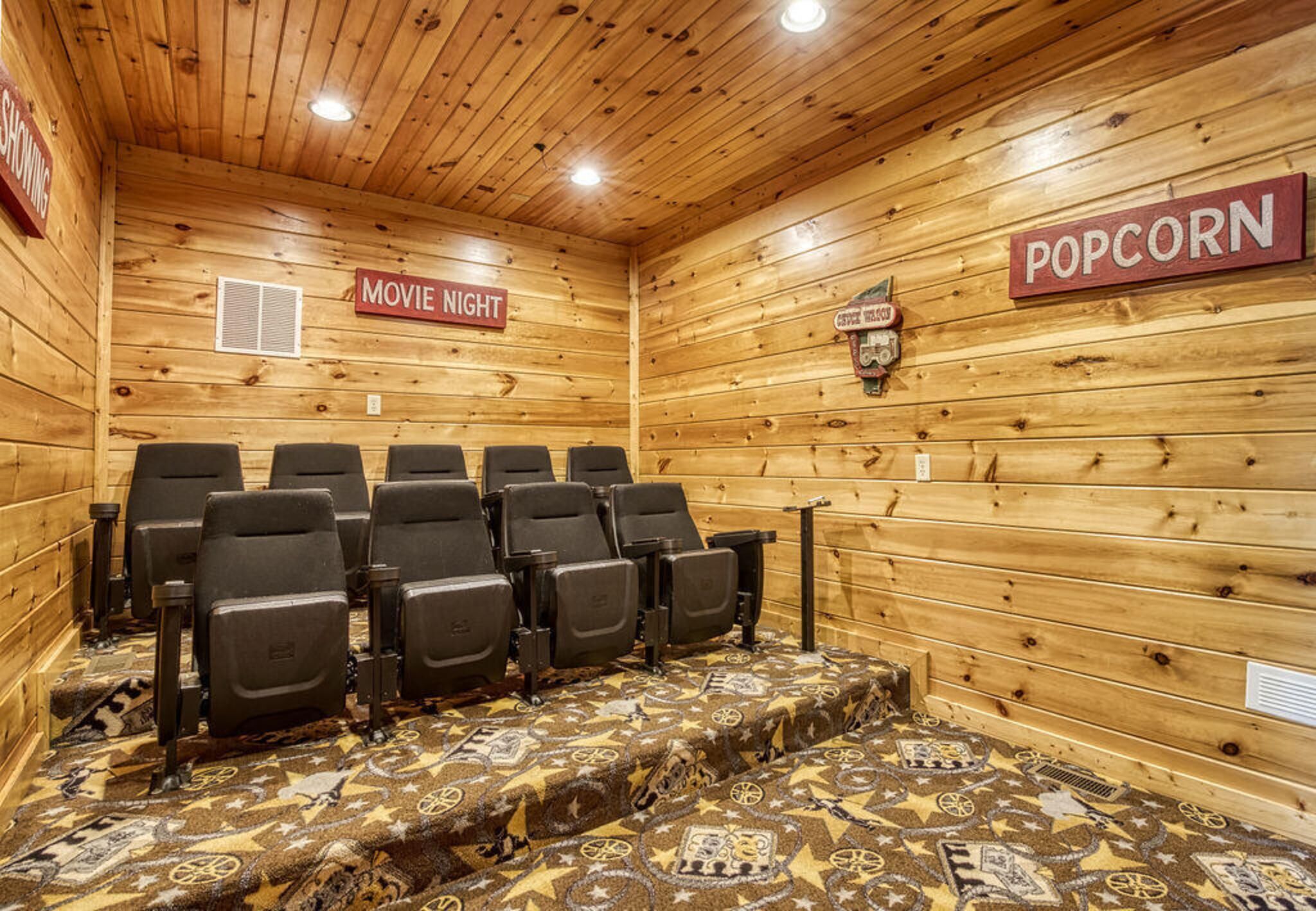 A wooden interior with a movie night sign, a popcorn sign, and rows of black chairs.