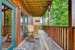 A wooden porch with rocking chairs and a railing, overlooking a forested area. - Bigfoot Hideout (Gatlinburg)