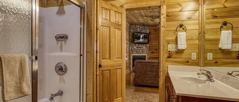 Un intérieur en bois comprenant une douche, un lavabo et un téléviseur fixé sur un mur en pierre.