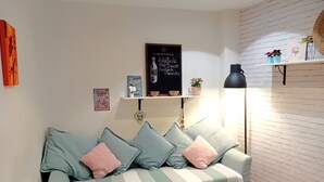 Una habitación con sofá, repisa con adornos, cartel enmarcados y lámpara.