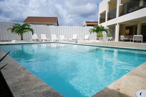 A swimming pool with white lounge chairs, a white fence, and a building with balconies. - Lovely 1-bedroom apartment in charming Noord (Noord)