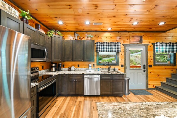 A modern kitchen with stainless steel appliances, wooden cabinets, and a central island. - Treetop Tranquility (Sevierville)
