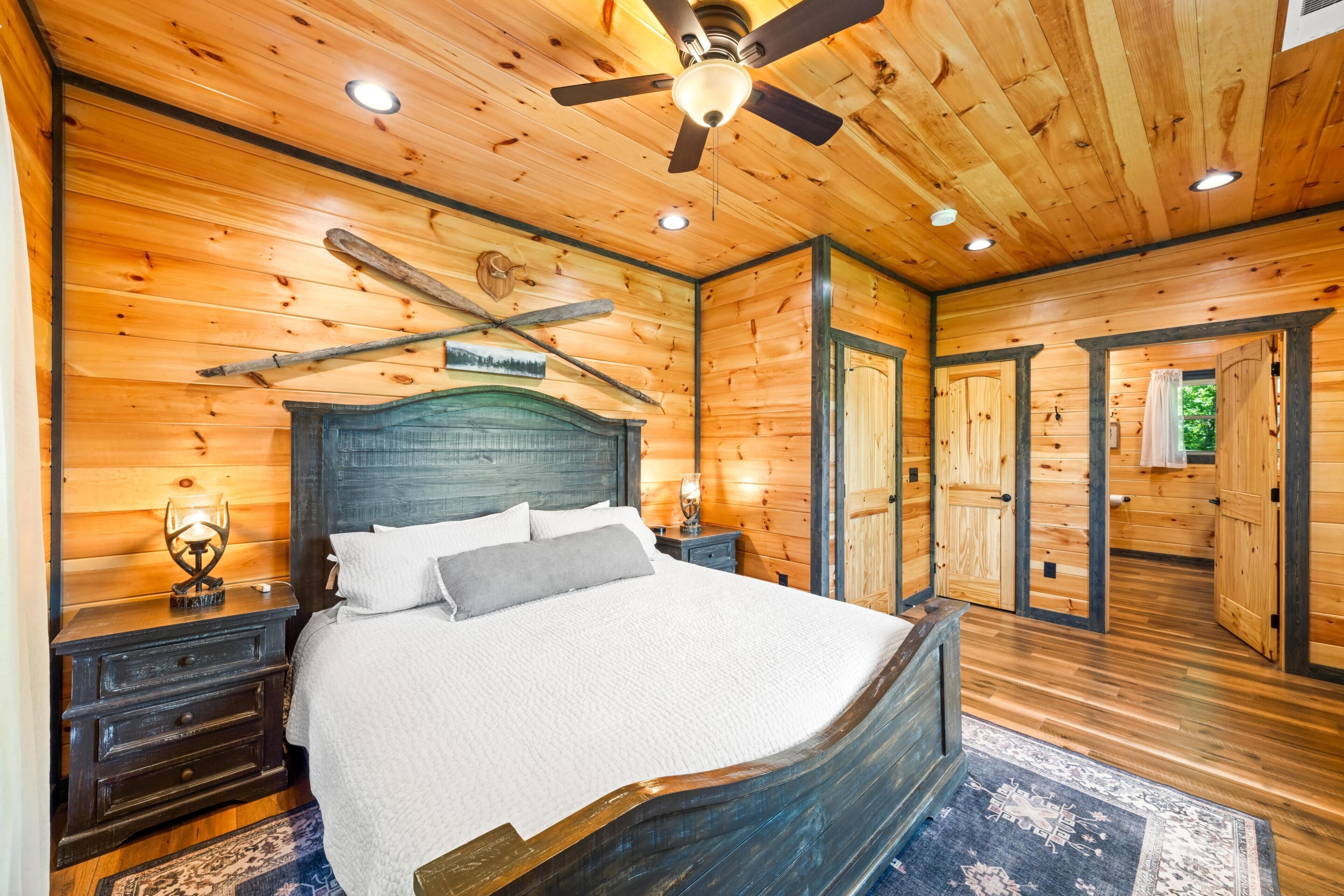Une chambre à coucher dans une cabane en bois, avec un lit, des tables de chevet, un ventilateur de plafond et une lampe de chevet.