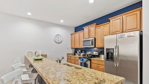 A kitchen with granite countertops, wooden cabinets, a stainless steel refrigerator, a microwave, and a clock on the wall. - NEW! Minutes to Disney World, Themed, Private Pool, Poolside Bar, Movie Theatre! (Kissimmee)