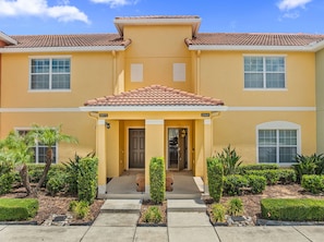 A two-story building with a yellow facade, a tiled roof, and a front porch with steps leading to the entrance. - NEW! Minutes to Disney World, Themed, Private Pool, Poolside Bar, Movie Theatre! (Kissimmee)