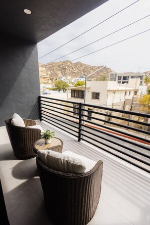 A balcony with wicker furniture and a view of buildings and hills. - Vista Pedregal Stylish Apt in Cabo Golden Zone (Cabo San Lucas)