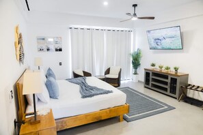 Ein Schlafzimmer mit Bett, Nachttisch, Lampe, Vorhängen, Fernseher und einer Pflanze.