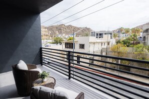 A balcony with wicker furniture, a potted plant, and a view of buildings and hills. - Vista Pedregal Stylish Apt in Cabo Golden Zone (Cabo San Lucas)
