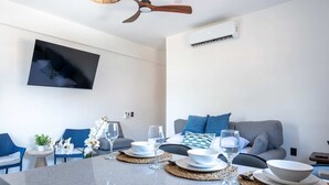 Una sala moderna con un televisor de pantalla plana, un ventilador de techo y un comedor con platos y vasos blancos.
