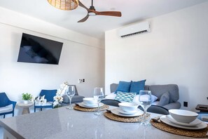 Ein modernes Wohnzimmer mit Flachbildfernseher, Deckenventilator und einem Essbereich, gedeckt mit weißen Tellern und Gläsern.