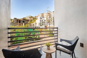 A balcony with wicker furniture and a small table with a plant, overlooking a cityscape with buildings and greenery. - Vista Pedregal New Apartment 5 min Walk to Marina (Cabo San Lucas)