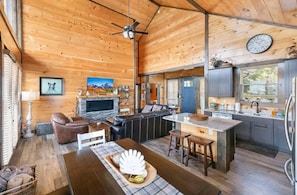 A cabin interior with a fireplace, wooden ceiling, kitchen area, and a dining table. - Picadilly Perch (Gatlinburg)