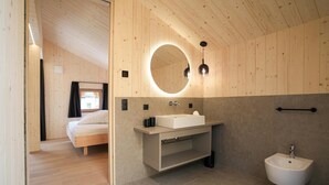 A modern bathroom with a wooden ceiling, a round mirror, a white sink, and a bidet. - Vrbo Property (Prateria)