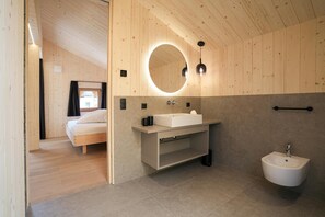 Un bagno moderno con soffitto in legno, uno specchio rotondo, un lavandino bianco e un bidet.