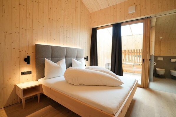Una camera da letto con testiera in legno, un comodino, un letto con cuscini e vista su uno spazio esterno tramite una porta scorrevole.