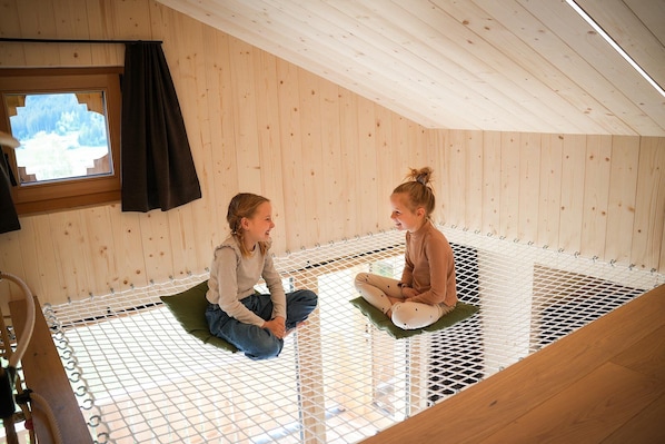 Two individuals seated on a netted platform in a room with wooden walls and a sloped ceiling.