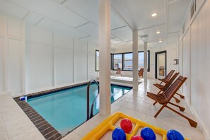 Una piscina interior amb parets de vidre transparent, gandules de fusta i una zona de jocs groga amb pilotes.