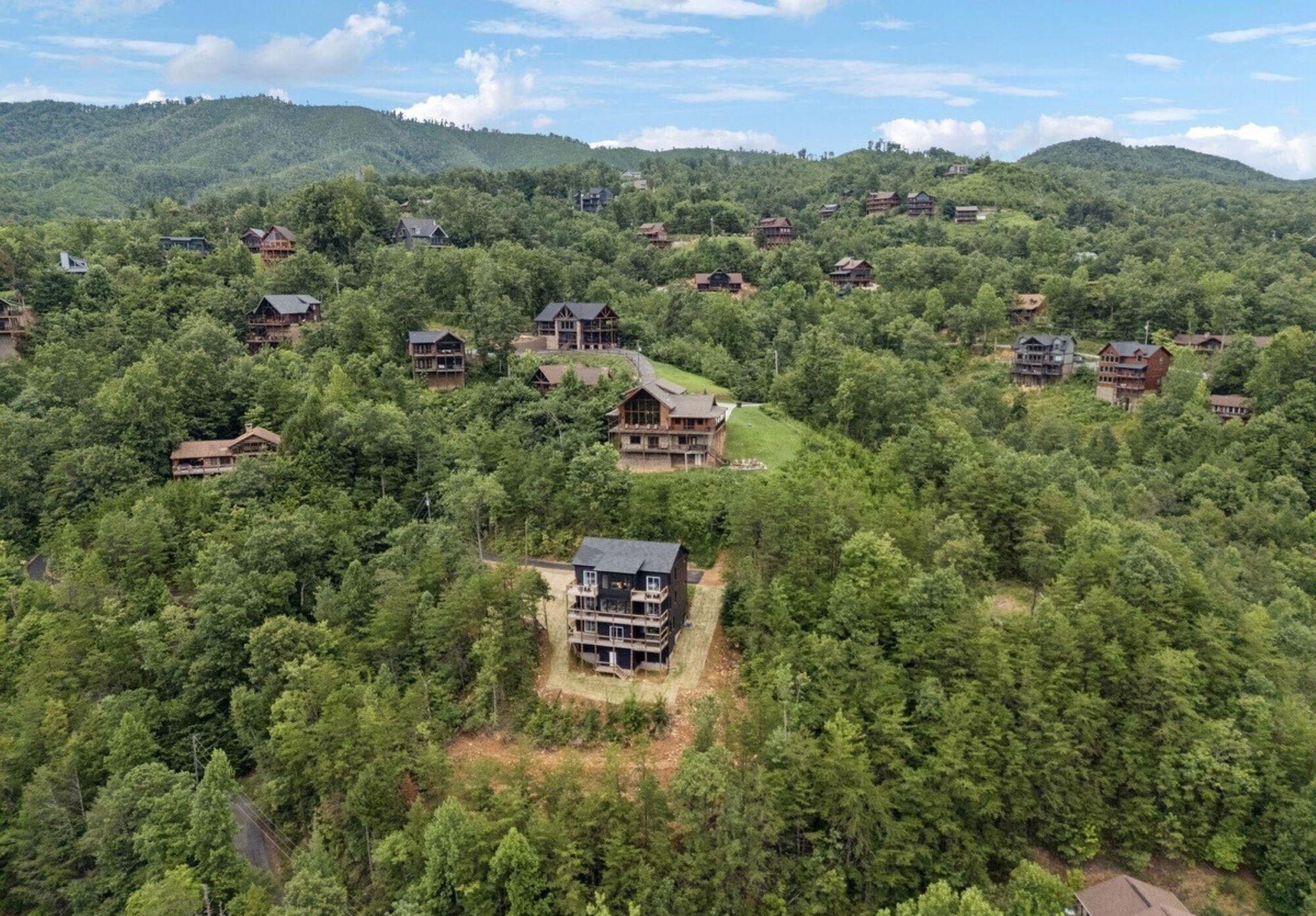 A cluster of log cabins surrounded by dense forest, with a prominent cabin featuring a large balcony and multiple levels.