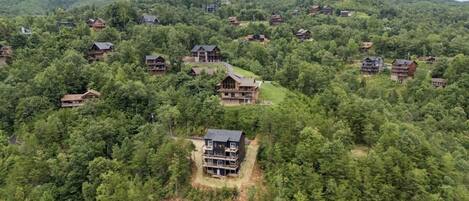 A cluster of log cabins surrounded by dense forest, with a prominent cabin featuring a large balcony and multiple levels.