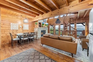 Ein Holzblockhaus-Interieur mit Essbereich, Sofa, Kamin und einer Wendeltreppe.