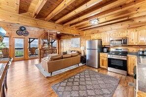 A wooden cabin interior with a living area, kitchen, and large windows. - Grand View Lodge (Sevierville)