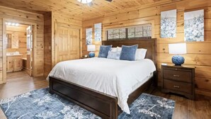 Een houten slaapkamer met een bed, nachtkastjes, een plafondventilator en kunstwerken aan de wanden.