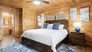 Un dormitorio de cabaña de madera con cama, mesitas de noche, ventilador de techo y cuadros en las paredes.