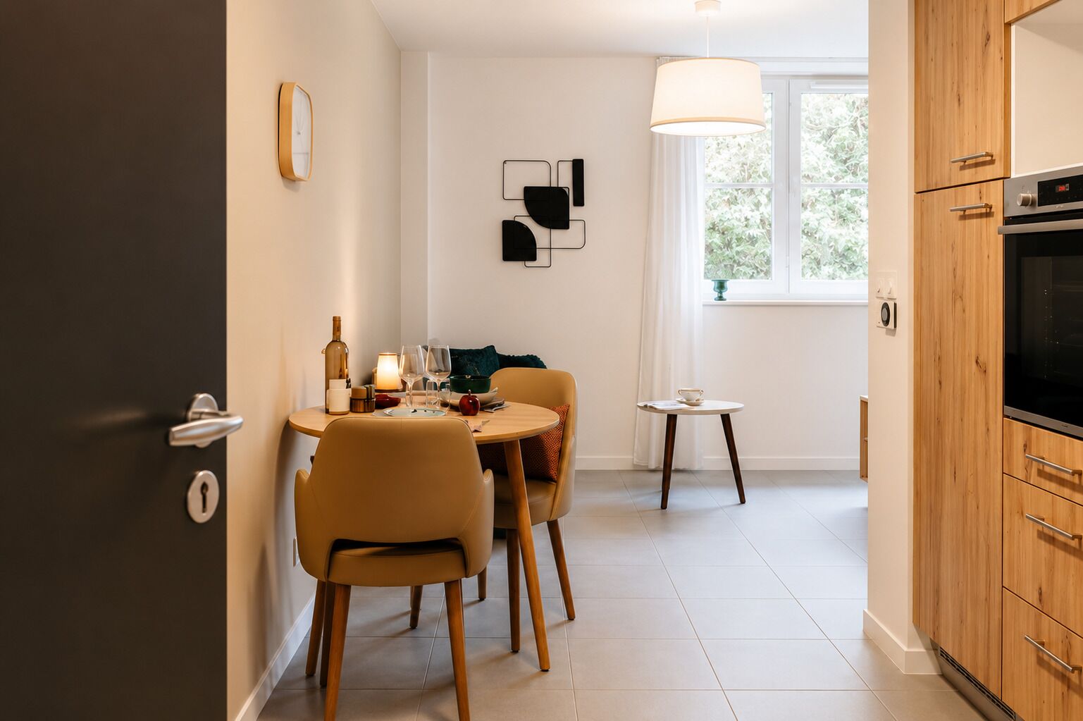 A modern kitchen with wooden cabinets, a dining area with a round table and chairs, and a window with a view of greenery.