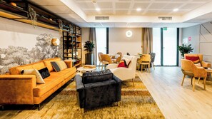 Un hall d’hôtel moderne avec un canapé, des fauteuils, une table basse, une bibliothèque et un coin repas.