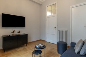 A living room with a flat-screen TV, a dark-colored sofa, a small round table, and a radiator. - Toscana 8 - FromHometoRome (Roma)