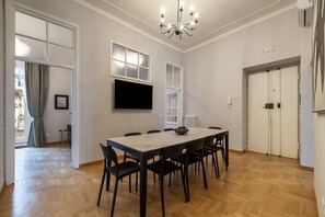 A dining area with a long table, chairs, a chandelier, a flat-screen TV, and a window. - Toscana 8 - FromHometoRome (Roma)