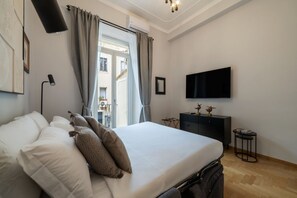 Ein Schlafzimmer mit einem Bett, einem Fernseher, einem Schreibtisch und einem Fenster mit Vorhängen.